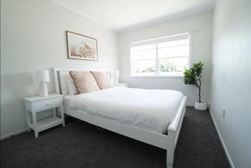 a white bedroom with a white bed and a window at Bright & Central Home in Auckland
