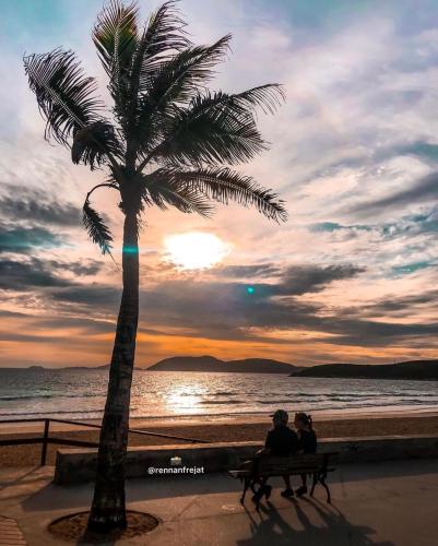 two people sitting on a bench next to a palm tree at Pousada Areias do Pero in Cabo Frio