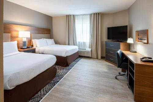 a hotel room with two beds and a desk and a television at Candlewood Suites Manassas by IHG in Manassas
