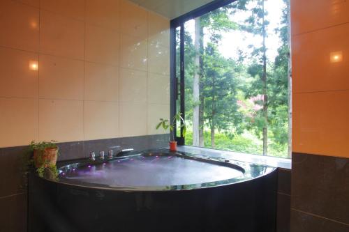 La salle de bains est pourvue d'une grande baignoire et d'une fenêtre. dans l'établissement HakubaGoryu Pension&LogCottage Arumu, à Hakuba