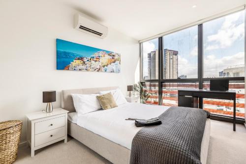 a bedroom with a bed and a desk and a window at KULA Docklands in Melbourne