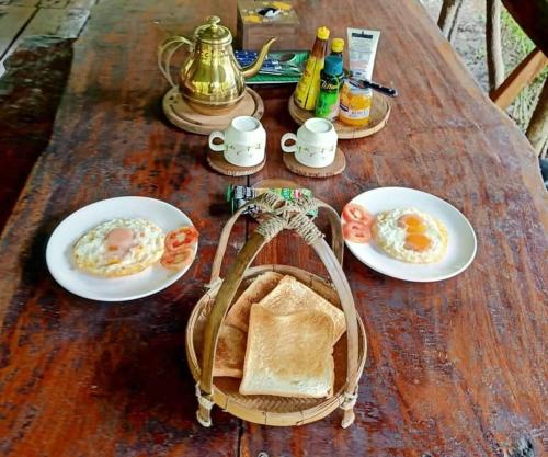 uma mesa de madeira com pratos de ovos e torradas em Koom Kachanaan em Ban Nong Thale