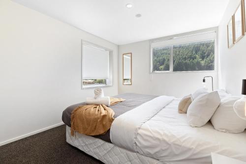 a white bedroom with a large bed with two windows at Central Mountain View Paradise in Queenstown
