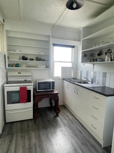 a kitchen with white appliances and a table with a microwave at Beach Front Cottage Napier in Napier