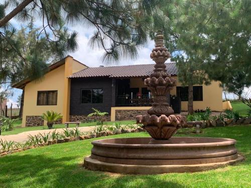 a fountain in the grass in front of a house at Cabaña No.2 Puerta del Bosque Mazamitla. in Mazamitla