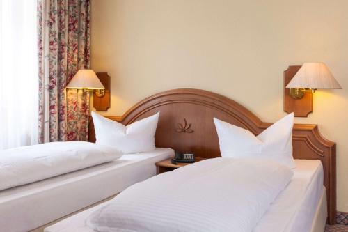 two beds in a hotel room with white pillows at Wyndham Garden Donaueschingen in Donaueschingen