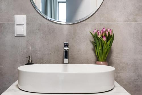 a bathroom sink with a mirror and a vase of pink flowers at Sol Marina Resort Wyspa Sobieszewska I - LoftAffair Collection in Wiślinka