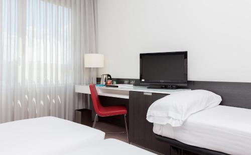 um quarto de hotel com uma secretária com uma televisão e uma cama em Axor Feria em Madri