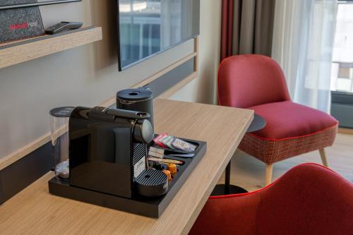 a hotel room with a coffee maker and a red chair at IntercityHotel Berlin Airport BER in Schönefeld