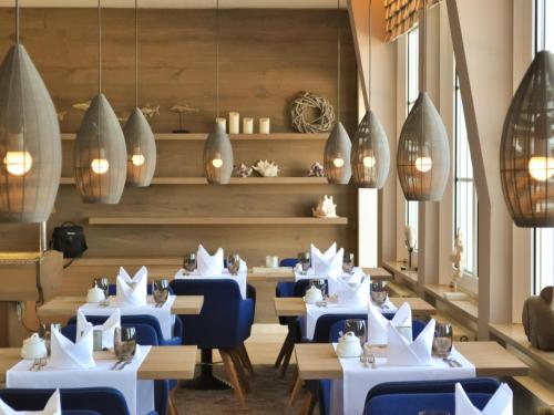 a restaurant with white tables and blue chairs at Strandhotel Miramar in Timmendorfer Strand