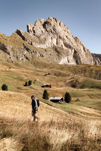 a person walking in a field with a mountain at Gardena Grödnerhof - Hotel & Spa in Ortisei
