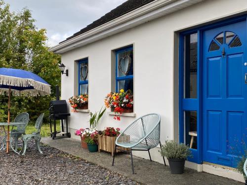 a house with a blue door and chairs and flowers at Lemonade cottages in Kilmurry McMahon