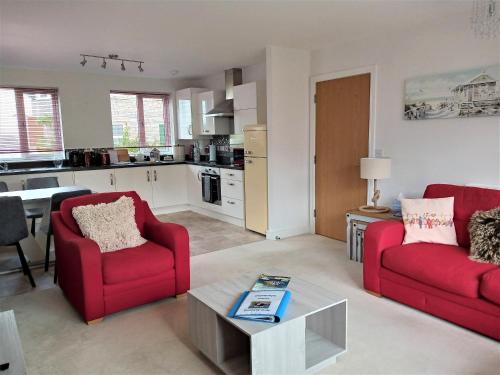 a living room with two red chairs and a kitchen at Stunning Apartment, balconies, private beach, coast path in Charlestown
