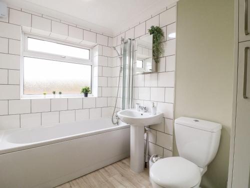 baño blanco con bañera, lavabo y aseo en The Crooked Cottage, en Ashbourne
