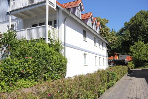 un edificio blanco con arbustos y flores junto a una acera en Haus zum Strand 2 4, en Wustrow