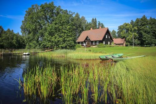 a house and a boat on the water near a lake at Guest House Mednieki in Salainis