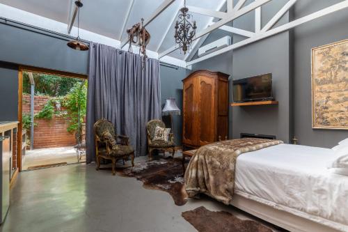 a bedroom with a bed and two chairs and a tv at Festina Lente Guesthouse in Johannesburg