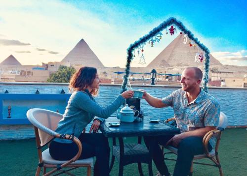 mężczyzna i kobieta siedzący przy stole z piramidami w tle w obiekcie Cheops Pyramids Inn w Kairze