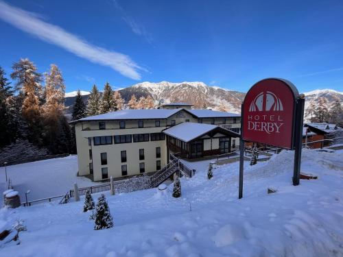 un hotel en la nieve con un cartel en el primer plano en Hotel Derby, en Folgarida