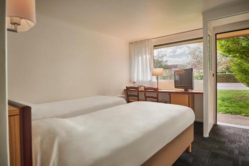 a room with two beds and a television and a window at Kyriad Direct Epinal in Épinal