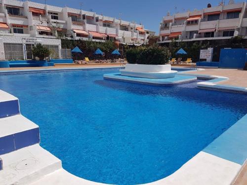 una grande piscina con acqua blu di fronte agli edifici degli appartamenti di EL CHAPARRAL Studio-appartement with fantastic pool view and STRONG WIFI a Costa Del Silencio