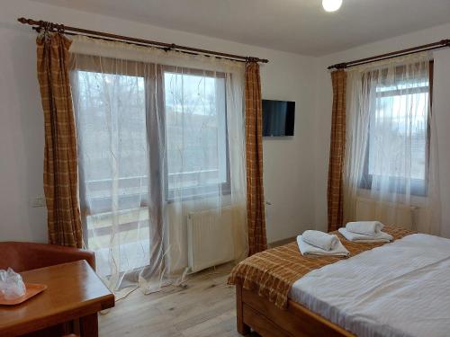 a bedroom with a bed and a table and windows at Casa Calea Haiducilor in Sohodol