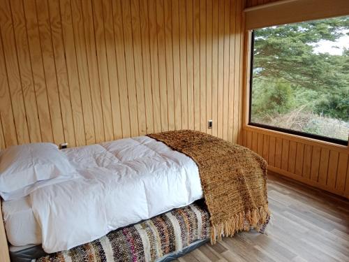 Cama en habitación de madera con ventana en Willipeuma en Yutuy
