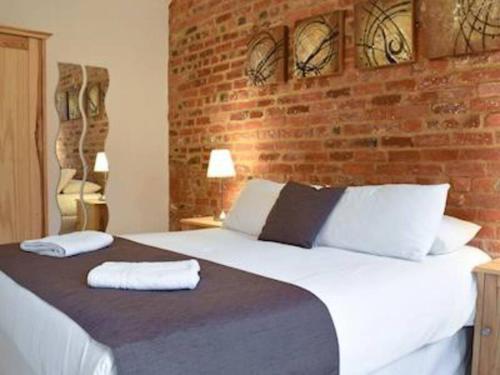 a bedroom with a large white bed with a brick wall at Mole Hole in Towcester