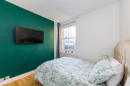 a room with a green wall with a couch and a tv at Indigo City Apartment in London