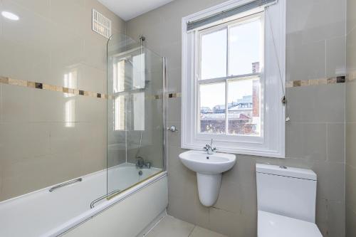 a white bathroom with a sink and a toilet and a window at Indigo City Apartment in London