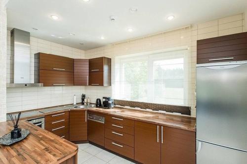 Una cocina con gabinetes de madera y un refrigerador de acero inoxidable. en 3-bedroom villa surrounded by beautiful nature, en Vaišvydava