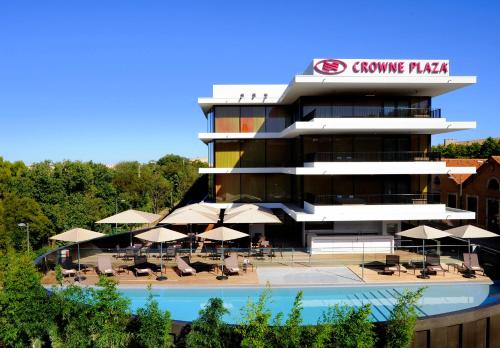 ein Gebäude mit einem Pool, Tischen und Sonnenschirmen in der Unterkunft Crowne Plaza Montpellier Corum, an IHG Hotel in Montpellier