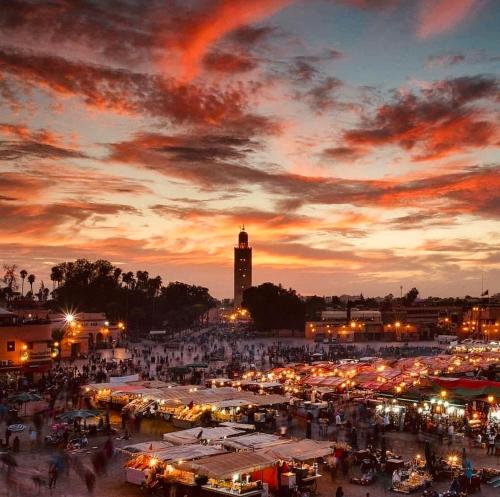 einen Markt mit einem Uhrturm im Hintergrund bei Sonnenuntergang in der Unterkunft Riad Allal in Marrakesch