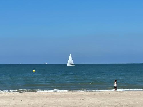 a person standing on the beach with a sail boat in the water at TOWNHOUSE TROUVILLE - Appart'Hotel & Studios in Trouville-sur-Mer
