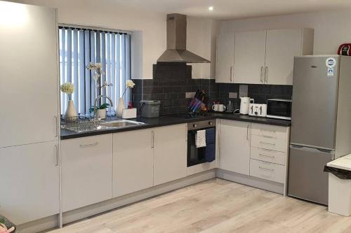 a kitchen with white cabinets and a stainless steel refrigerator at Daisy Lodge - Spacious Two Bed Flat - Parking, Netflix, WIFI - Close to Blenheim Palace & Oxford - F1 in Kidlington