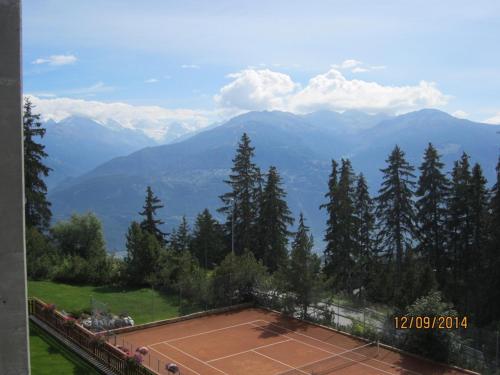 a tennis court with trees and mountains in the background at Residence Cransalpin in Crans-Montana