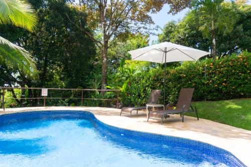 a swimming pool with two chairs and an umbrella at Arbol Verde Villas in Ojochal