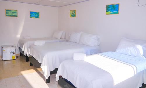 a room with three beds with white sheets at Hotel Posada Enilda in Providencia