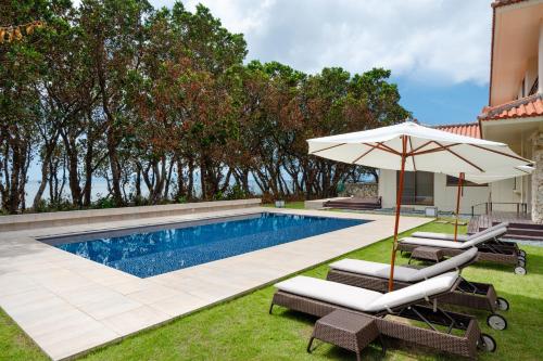 einen Pool mit einem Sonnenschirm und Stühlen sowie einem Pool in der Unterkunft Ocean Front Villa Ishigakijima Ⅰ in Ishigaki-jima