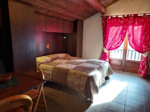 1 dormitorio con 1 cama con cortinas rojas y mesa en Lauson, en Cogne