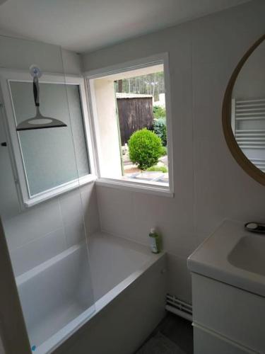 La salle de bains blanche est pourvue d'une baignoire et d'une fenêtre. dans l'établissement Maisonnette Les Palombes, à Lacanau