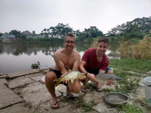 two men holding fish in front of a lake at Tuyet's hostel in Ninh Binh