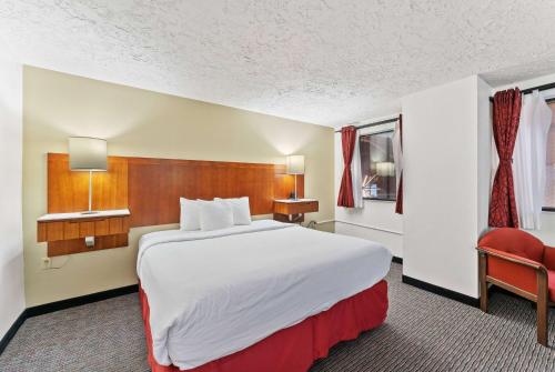 a hotel room with a large bed and a red chair at Ramada by Wyndham Cedar City in Cedar City