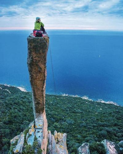 a man sitting on top of a rock on the ocean at Villa Settimia a 50 mt dalla spiaggia! in Àrbatax