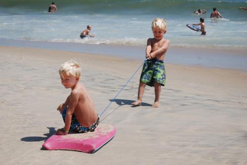 two young boys on the beach playing with a surfboard at Tides Inn in Ocean City