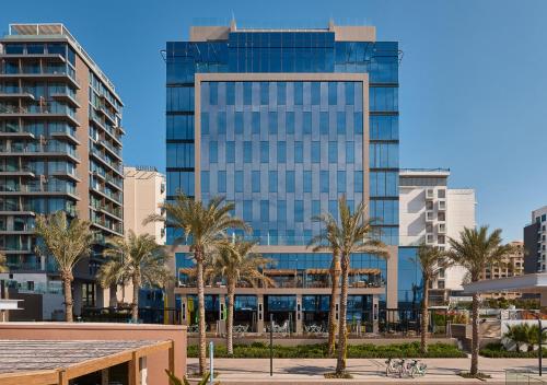 a tall glass building with palm trees in front of it at voco Dubai The Palm by IHG in Dubai
