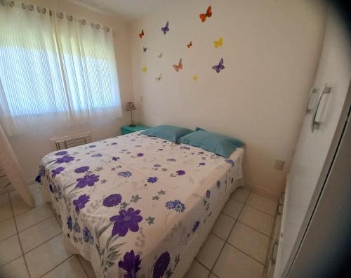 1 dormitorio con 1 cama con flores púrpuras y mariposas en la pared en Apto de cobertura na praia da Cachoeira, en Florianópolis