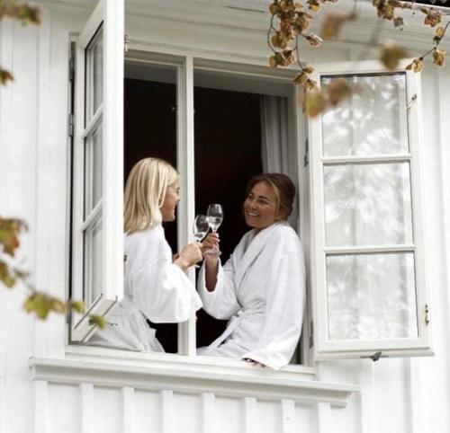 two women in white robes holding a glass of wine on a window at Engø Gård Hotel & Restaurant in Tjøme