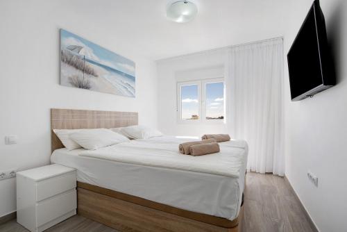 a white bedroom with a bed and a flat screen tv at Casa Helieta in Puerto del Rosario