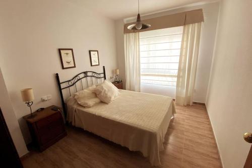 een slaapkamer met een bed met witte lakens en een raam bij Apartamento a unos pasos de la Playa (Rota) in Rota